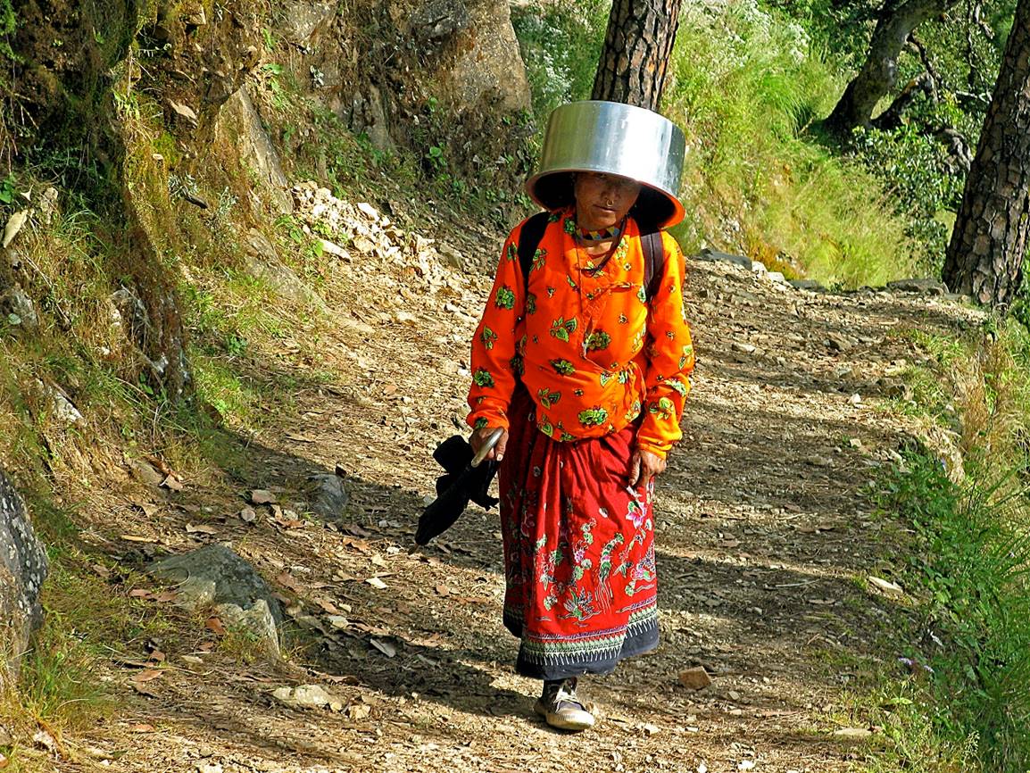 A person walking on a path with a pot on her head

Description automatically generated