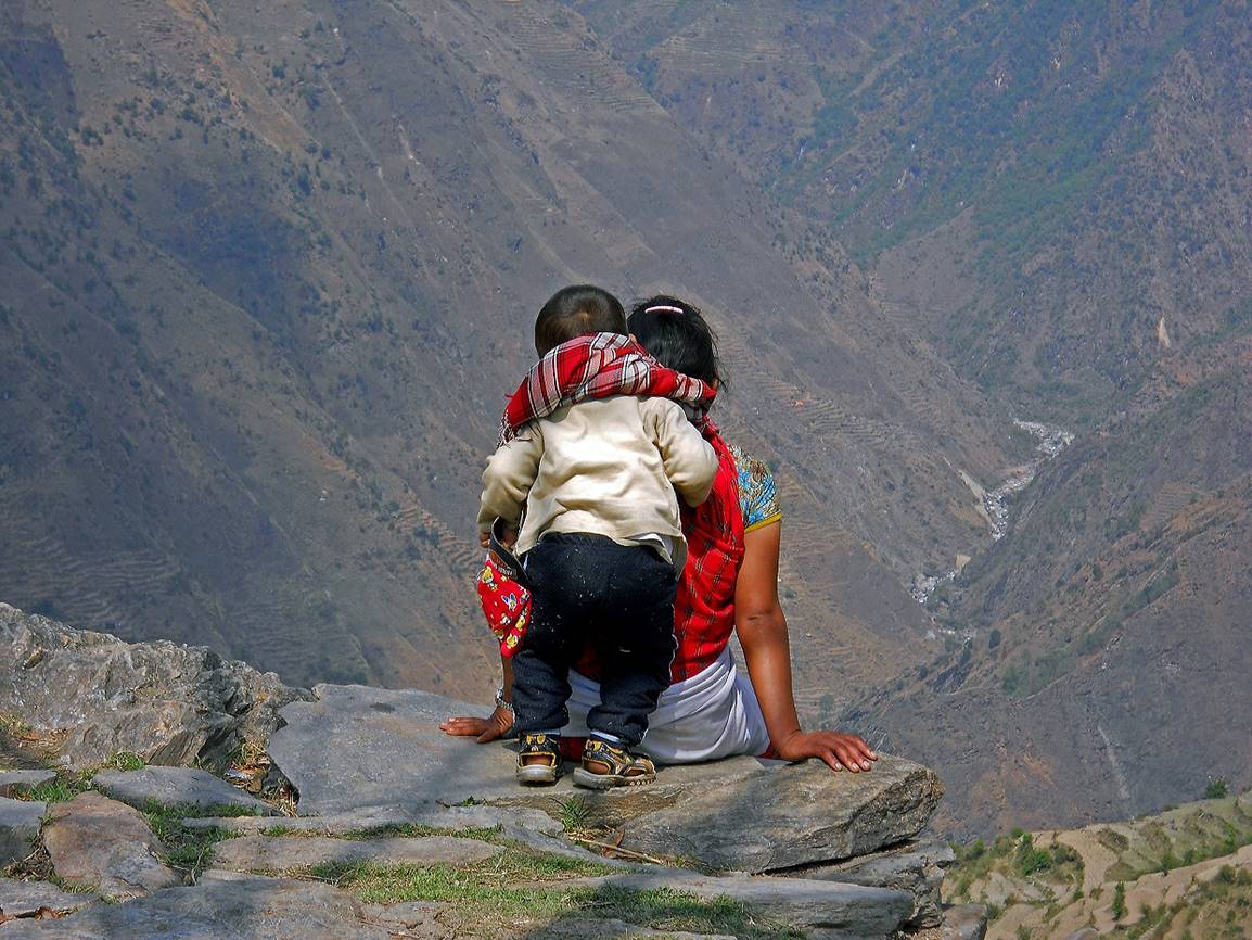 A person and child sitting on a rock looking at a valley

Description automatically generated