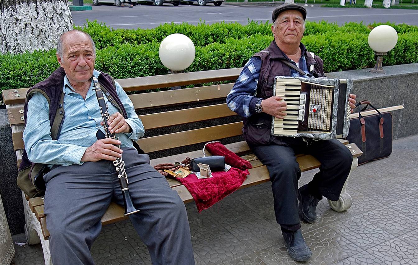 A couple of men sitting on a bench playing instruments

Description automatically generated