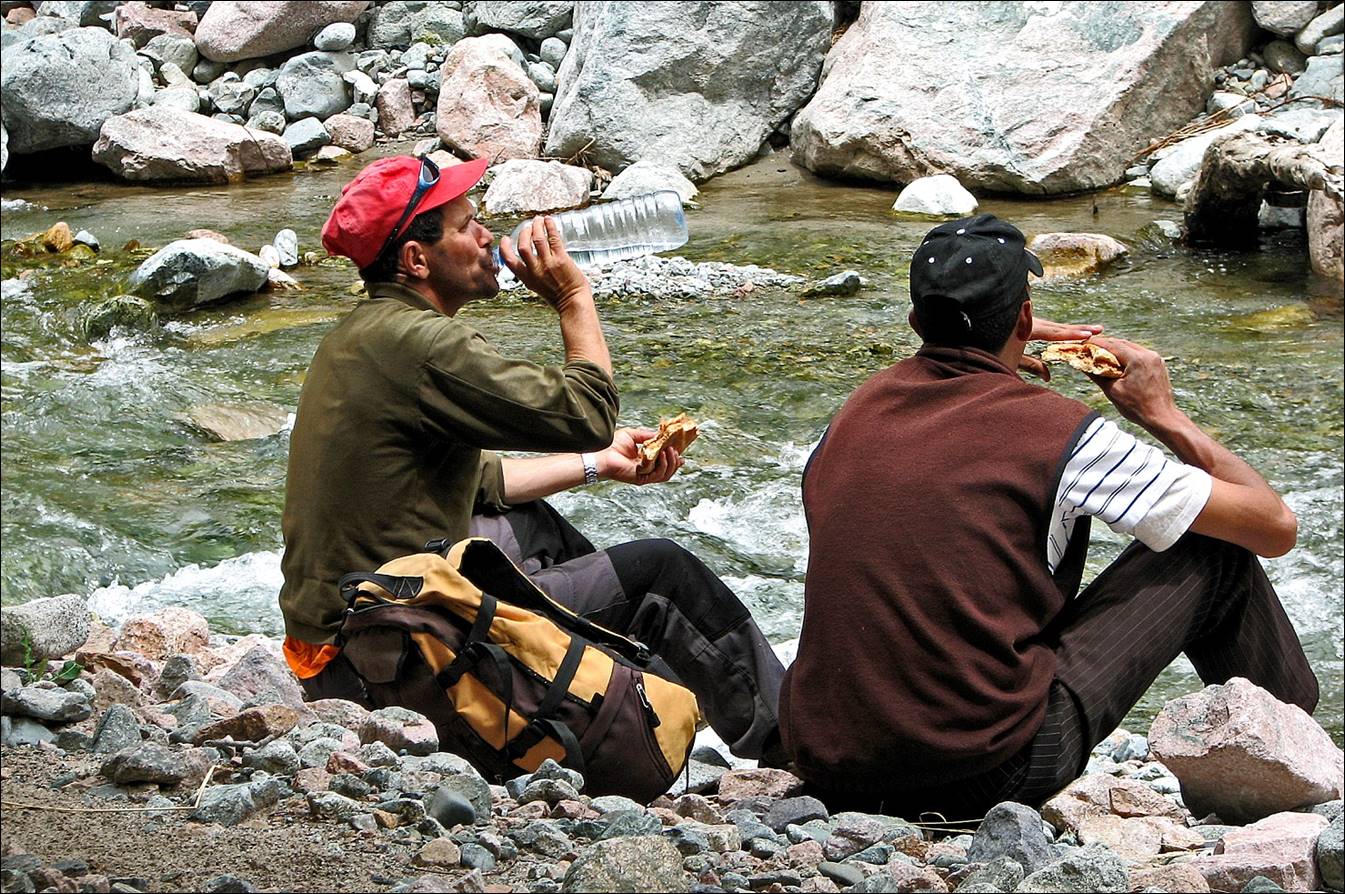 A couple of men sitting on a rocky shore eating food

Description automatically generated