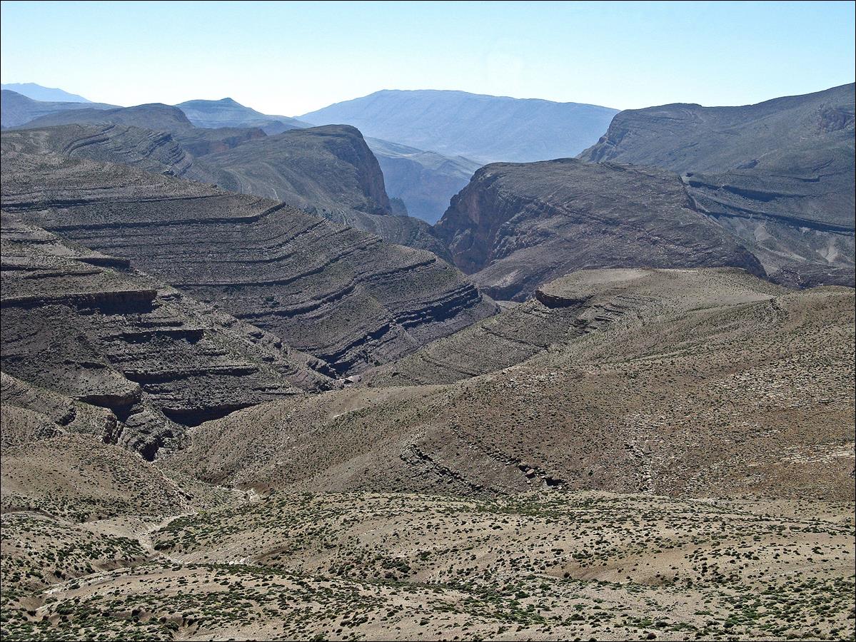 A large rocky canyon with mountains in the background

Description automatically generated
