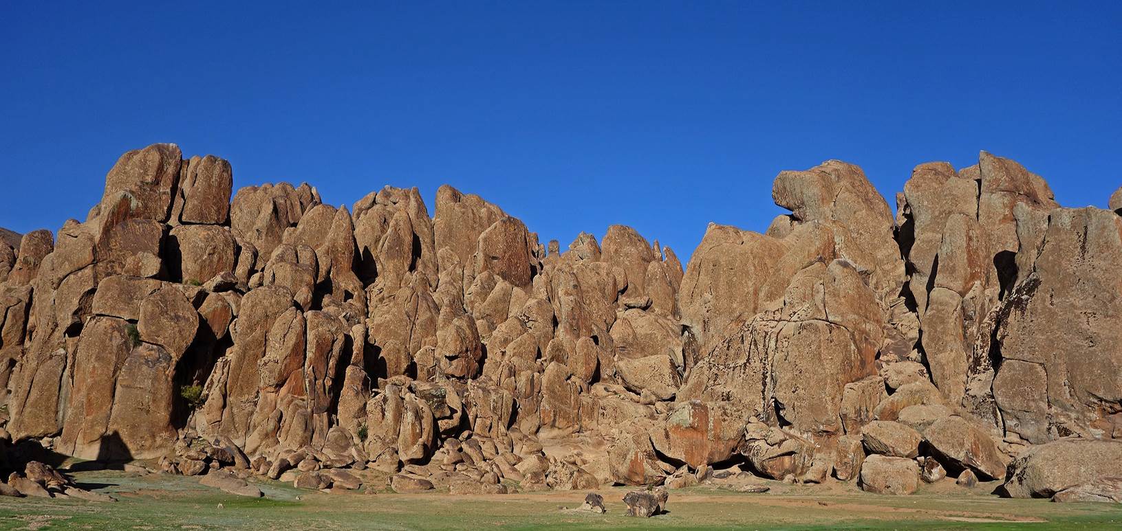 A large rock formation with blue sky with Smith Rock State Park in the background

Description automatically generated