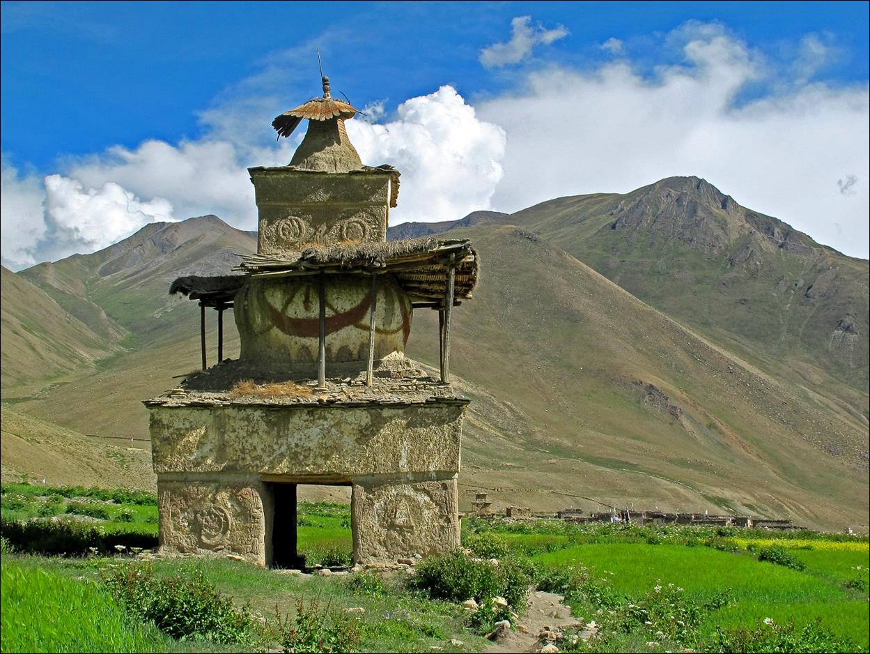 A stone building in a field with mountains in the background

Description automatically generated