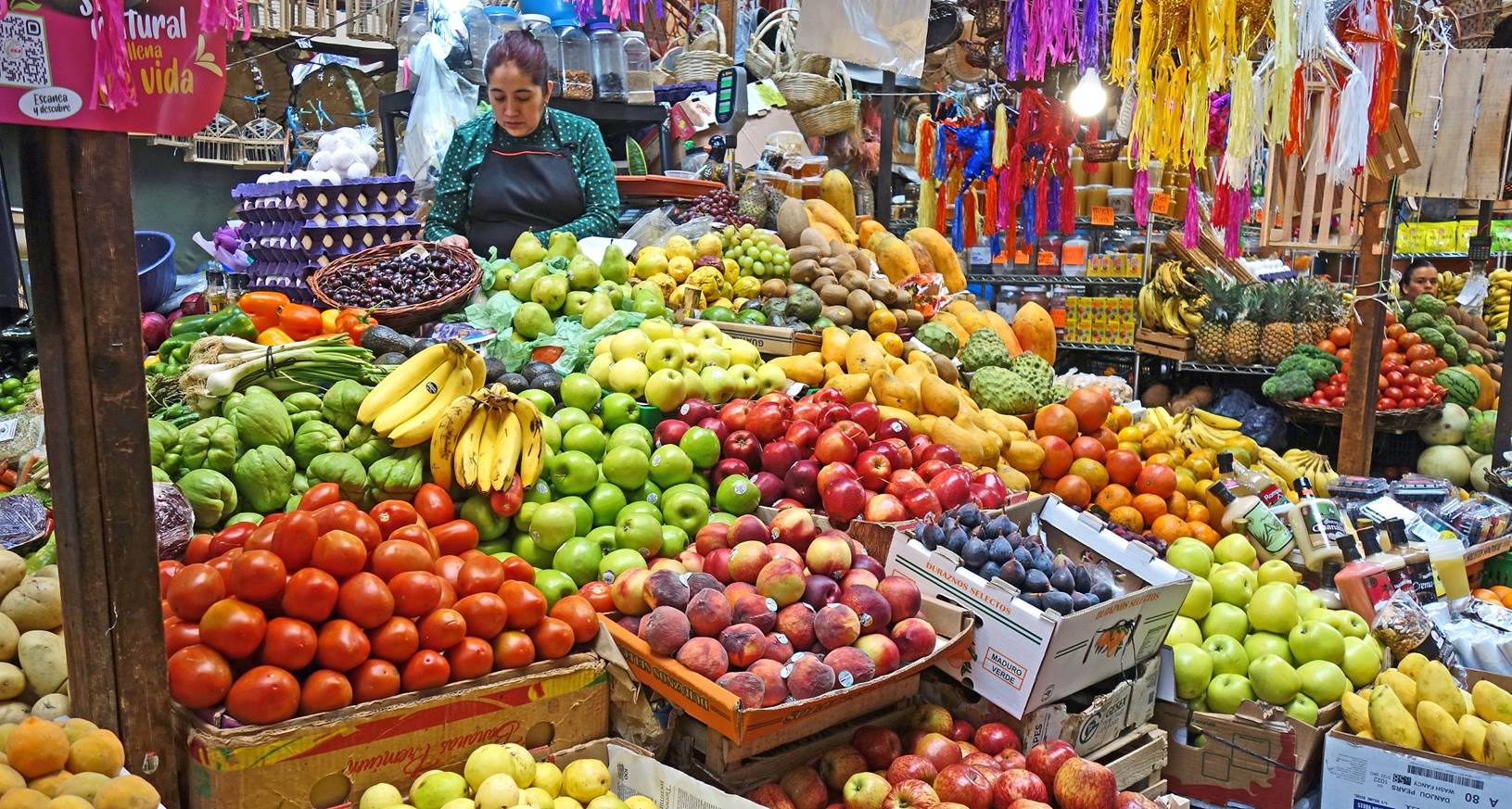 A person standing in a market with many different fruits

Description automatically generated